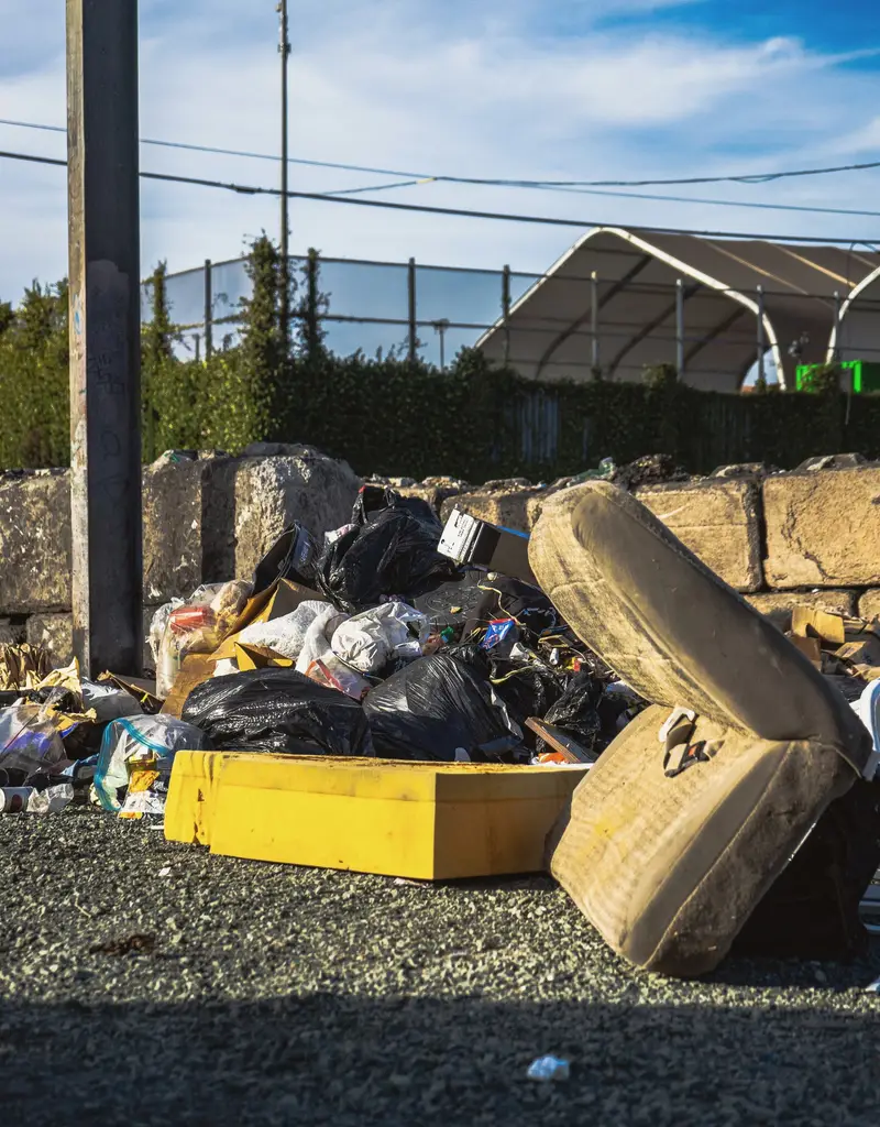Black bin bags and an old mattress dumped beside a fence on waste ground