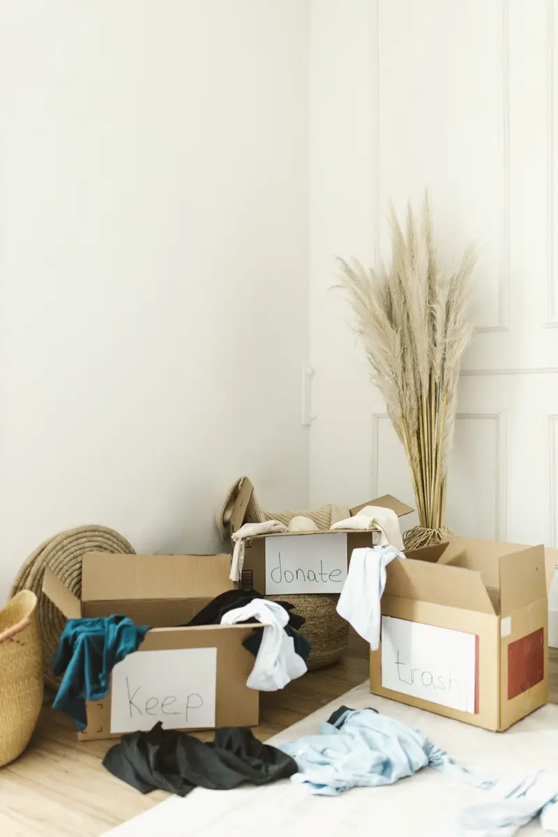 Cardboard boxes and clothes sorted on a bedroom floor during a clear-out