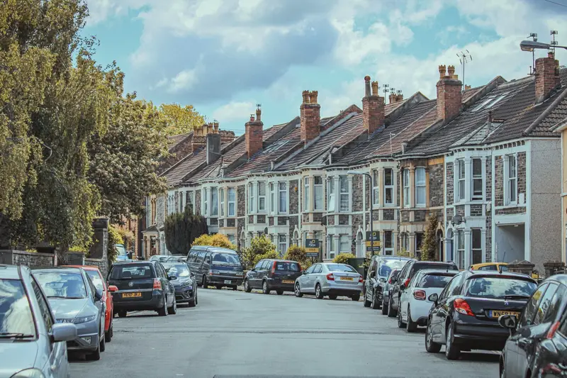 A row of British terraced houses with cars parked along the street